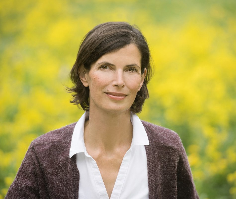 Heilpraktikerin für Psychotherapie und Paartherapeutin Christina Pielken sitzt lächelnd vor einem Rapsfeld. Sie arbeitet mit ihren Patient*innen auf Wunsch auch gerne draußen in der Natur (Outdoor).