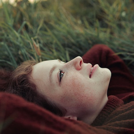 Eine Frau liegt im Gras auf dem Rücken, die Arme hinter dem Kopf verschränkt. Sie steht symbolisch für die Progressive Muskelentspannung.
