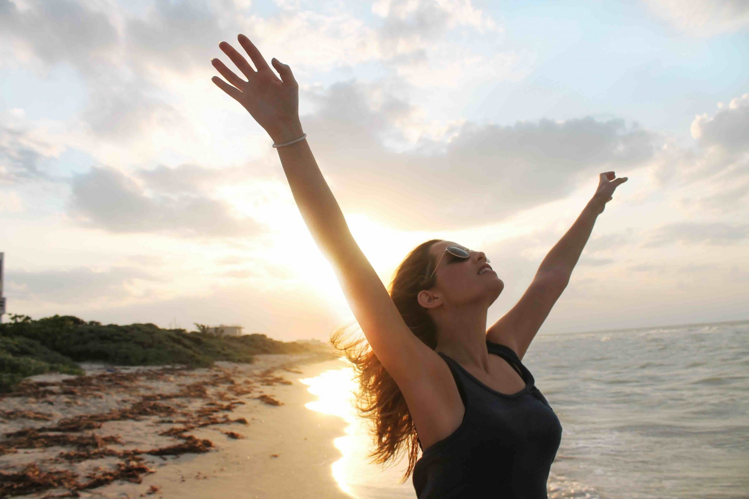 Frau am Strand happy mit ausgebreiteten Armen